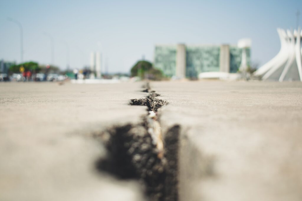 Close-up of a cracked pavement with buildings in the blurred background, emphasizing urban decay.