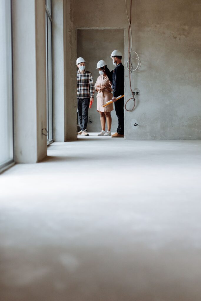 Realtors and clients wearing hard hats exploring a modern construction site indoors.